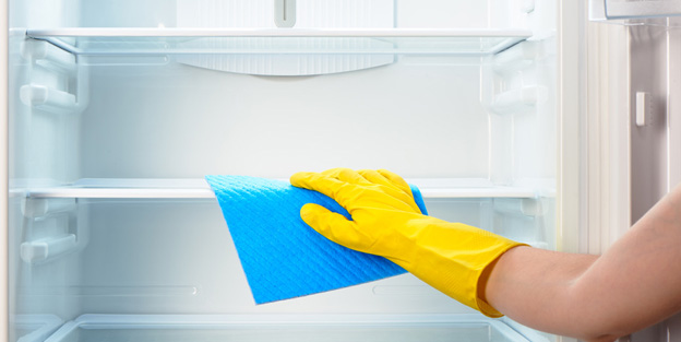 Woman's hand in yellow glove cleaning refrigerator with blue rag